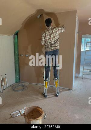 Arbeiter auf Stelzen Verputzen einer Mauer in einem Gebäude Renovierung in Rural Devon, England, Großbritannien Stockfoto