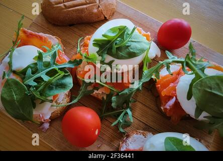 Pochiertes Ei auf gegrilltem Toast mit geräuchertem Lachs, Rucola und Gemüse auf Weißbrett. Gesundes Frühstück Stockfoto