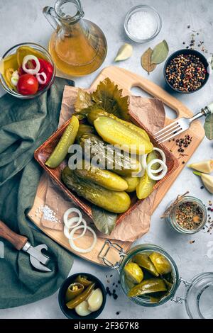 Holzplatte mit Gurken auf grauem Hintergrund mit Zwiebeln, Knoblauch, Lorbeerblatt und Gewürzen. Vertikale Ansicht. Stockfoto