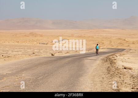 Eine Frau fährt mit dem Fahrrad entlang der Ruta a Lagunillas, mitten in der Wüste, in der Nähe von Playa Las Minas im Paracas National Reserve, Pisco, Departement Stockfoto