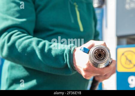 Alter Mann in einem grünen Pullover und Jeans mit einem komprimierten Erdgas (CNG) Füllschlauch, um den Tank des Öko-Autos zu füllen. Ökologisches Konzept. Stockfoto