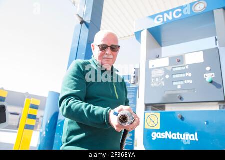 Älterer Mann in grünem Pullover und Jeans mit einem komprimierten Erdgas (CNG) Füllschlauch, um den Tank des Öko-Autos zu füllen. Mit der Gaspumpe hinter ihm Stockfoto