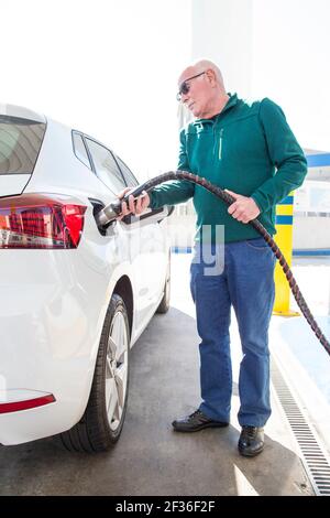 Älterer Mann mit grünem Pullover, der mit cng (komprimiertes Erdgas) in seinem umweltfreundlichen Auto auffüllt. Konzept für saubere Energie. Stockfoto