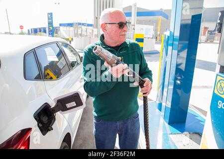 Alter Mann in einem grünen Pullover und Jeans mit einem komprimierten Erdgas (CNG) Füllschlauch, um den Tank des Öko-Autos zu füllen. Ökologisches Konzept. Stockfoto