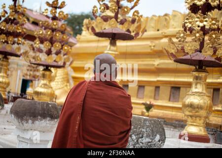 BAGAN, NYAUNG-U, MYANMAR - 2. JANUAR 2020: Ein buddhistischer Mönch in einer roten Robe und Brille beobachtet eine berühmte goldene Stupa-Pagode an einem historischen Ort Stockfoto