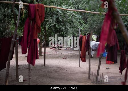 BAGAN, NYAUNG-U, MYANMAR - 2. JANUAR 2020: Ein paar junge Mönche sitzen auf dem Boden in einem Wald Clearance hinter einigen buddhistischen roten Roben hängen Stockfoto