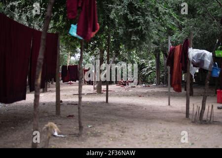 BAGAN, NYAUNG-U, MYANMAR - 2. JANUAR 2020: Ein paar junge Mönche sitzen auf dem Boden in einem Wald Clearance hinter einigen buddhistischen roten Roben hängen Stockfoto