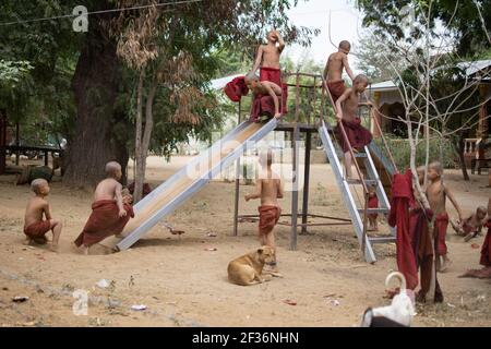 BAGAN, NYAUNG-U, MYANMAR - 2. JANUAR 2020: Junge Mönche spielen, laufen, springen, klettern, lachen und haben gemeinsam Spaß auf einem lokalen Spielplatz mit einer Rutsche Stockfoto