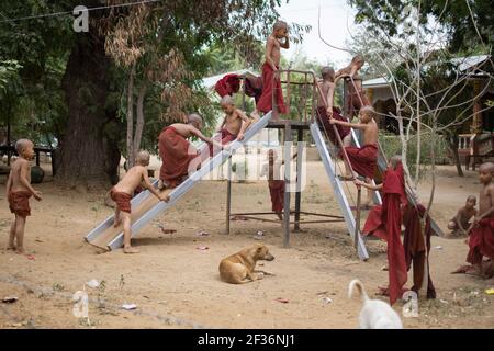 BAGAN, NYAUNG-U, MYANMAR - 2. JANUAR 2020: Junge Mönche spielen, laufen, springen, klettern, lachen und haben gemeinsam Spaß auf einem lokalen Spielplatz mit einer Rutsche Stockfoto