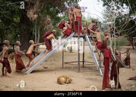 BAGAN, NYAUNG-U, MYANMAR - 2. JANUAR 2020: Junge Mönche spielen, laufen, springen, klettern, lachen und haben gemeinsam Spaß auf einem lokalen Spielplatz mit einer Rutsche Stockfoto