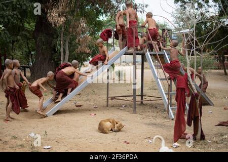 BAGAN, NYAUNG-U, MYANMAR - 2. JANUAR 2020: Junge Mönche spielen, laufen, springen, klettern, lachen und haben gemeinsam Spaß auf einem lokalen Spielplatz mit einer Rutsche Stockfoto