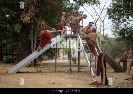 BAGAN, NYAUNG-U, MYANMAR - 2. JANUAR 2020: Junge Mönche spielen, laufen, springen, klettern, lachen und haben gemeinsam Spaß auf einem lokalen Spielplatz mit einer Rutsche Stockfoto