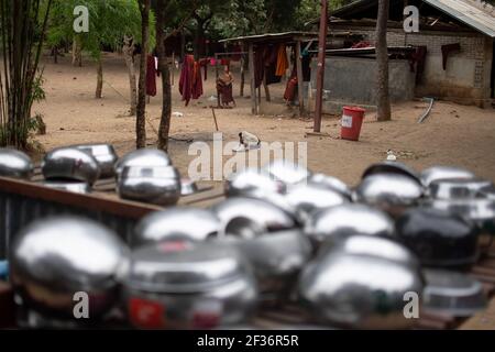BAGAN, NYAUNG-U, MYANMAR - 2. JANUAR 2020: Rote buddhistische Roben hängen und glänzende Almosenschalen trocknen, während zwei junge Mönche im Hintergrund spazieren Stockfoto