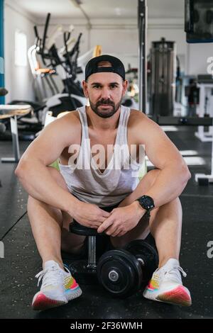 Junger Mann, der im Fitnessstudio sitzt und die Hanteln ausruhen. Stockfoto