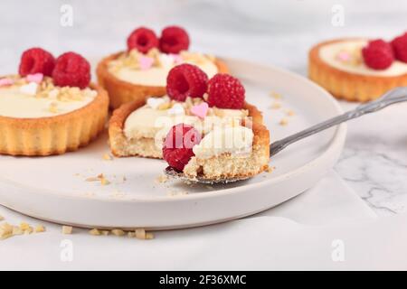Kleine Tartelteiggebäck mit weißer Sahne, gekrönt mit Himbeerfrüchten und Mandelstreuseln Stockfoto