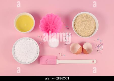 Backzutaten und Werkzeuge wie Puderzucker, gemahlene Mandeln, Eiweiß, Salz, Zuckerstreuseln und Kuchenform auf rosa Hintergrund Stockfoto