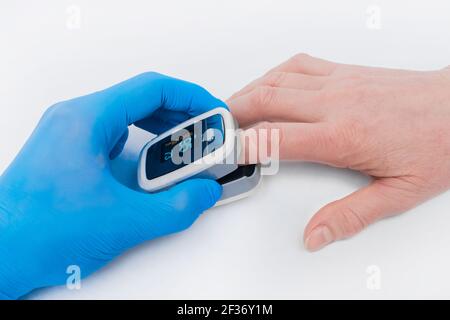 Die Hand des Arztes in einem medizinischen Latexhandschuh hält ein Gerät, um Sauerstoff im Blut zu messen, Pulsexymeter mit dem Finger einer älteren Frau auf einem weißen Stockfoto