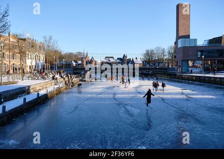 Amersfoort, Niederlande - 13. Feb 2021: Eislaufen auf gefrorenem Kanal der Eem im Stadtzentrum von Amersfoort mit dem berühmten Koppelpoort in der Stockfoto