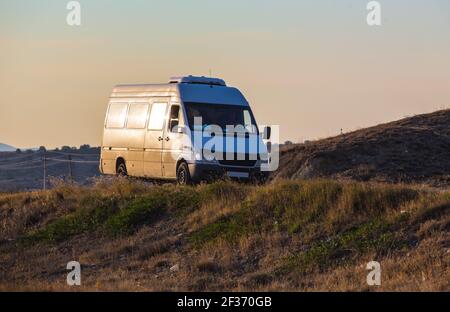 Minivbus bewegt sich bei Sonnenuntergang auf den Hügeln auf der Straße Stockfoto