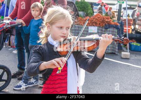 2019-10-19 Bloomington USA - kleines Mädchen, das sich auf das Geigenspielen auf dem Bauernmarkt konzentriert, während ein kleiner Junge mit Eltern sie anschaut. Stockfoto