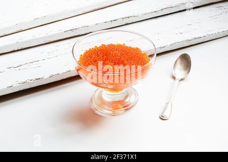 Roter Lachskaviar in einem durchsichtigen Glas und einem Silber Löffel auf einem weißen Tisch Stockfoto