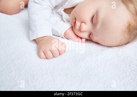 Niedliches Baby schläft süß auf weißer Bettwäsche in weißer Kleidung. Nahaufnahme. Schöne, gesunde, weiche Haut, lange Wimpern. Speicherplatz kopieren. Stockfoto