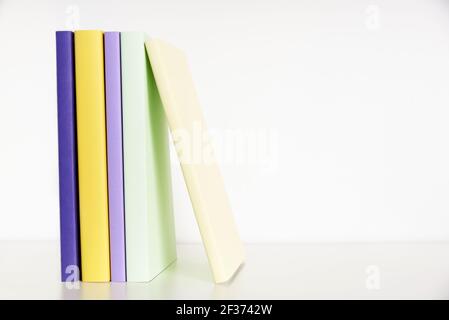 Farbige Bücher mit leerem Rücken auf einem weißen Regal mit weißem Hintergrund. Konzepte des Lesens und der Bildung. Helles Bild mit Kopierbereich. Stockfoto