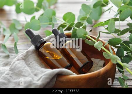 Zwei Flaschen ätherisches Eukalyptus-Öl in Holzschale und Eukalyptus-Zweige auf dem Tisch. Alternative Medizin. Stockfoto