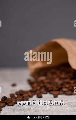 Nahaufnahme von frisch gerösteten Kaffeebohnen in der Nähe von Wort AMERICANO mit kleinen weißen Würfel geschrieben. Draufsicht. Stockfoto