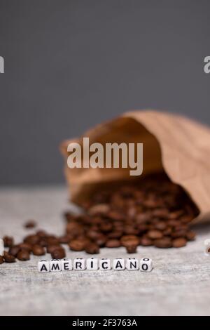 Nahaufnahme von frisch gerösteten Kaffeebohnen in der Nähe von Wort AMERICANO mit kleinen weißen Würfel geschrieben. Draufsicht. Stockfoto