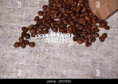 Nahaufnahme von frisch gerösteten Kaffeebohnen in der Nähe von Wort AMERICANO mit kleinen weißen Würfel geschrieben. Draufsicht. Stockfoto