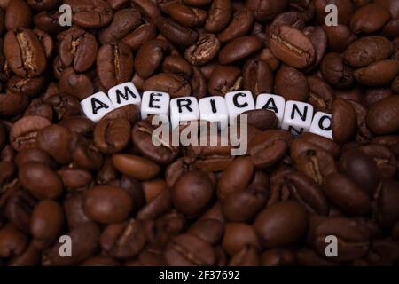 Nahaufnahme von frisch gerösteten Kaffeebohnen in der Nähe von Wort AMERICANO mit kleinen weißen Würfel geschrieben. Draufsicht. Stockfoto