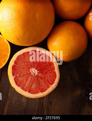 Nahaufnahme von reifen Grapefruitscheiben und mehreren ganzen Orangen Auf braunem rustikalem Holztisch mit Kopierraum Stockfoto