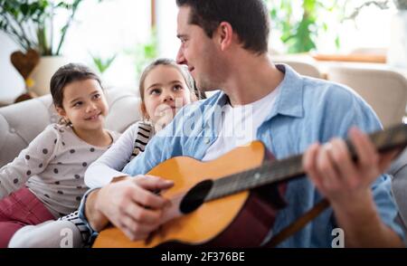 Vater mit kleinen Töchtern, die zuhause auf dem Sofa sitzen und Gitarre spielen. Stockfoto