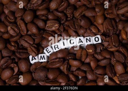 Nahaufnahme von frisch gerösteten Kaffeebohnen in der Nähe von Wort AMERICANO mit kleinen weißen Würfel geschrieben. Draufsicht. Stockfoto