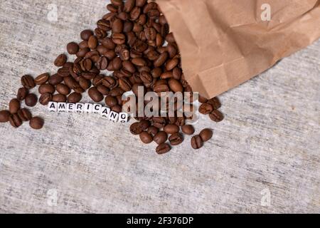 Nahaufnahme von frisch gerösteten Kaffeebohnen in der Nähe von Wort AMERICANO mit kleinen weißen Würfel geschrieben. Draufsicht. Stockfoto
