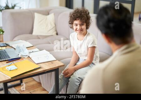 Glücklicher lateinischer Junge, der mit seinem Vater kommuniziert, Hausaufgaben macht, während er im Wohnzimmer zu Hause studiert Stockfoto