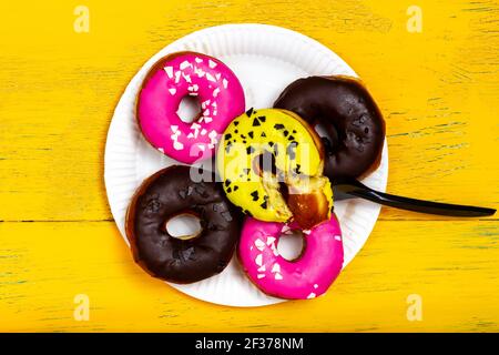 Ein voller Teller mit Donuts. Viele farbige Donuts auf einem Pappteller. Blick von oben. Stockfoto