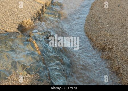 Frisches Regenwasser sickert aus dem Sand und schneidet einen Weg zum Meer in der Carlyon Bucht außerhalb von St. Austell, Cornwall, England Stockfoto