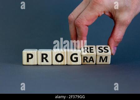 Fortschritts- und Programmsymbol. Geschäftsmann dreht Holzwürfel und ändert das Wort "Programm" in "Fortschritt". Schöner grauer Hintergrund. Geschäft, Prognosen Stockfoto