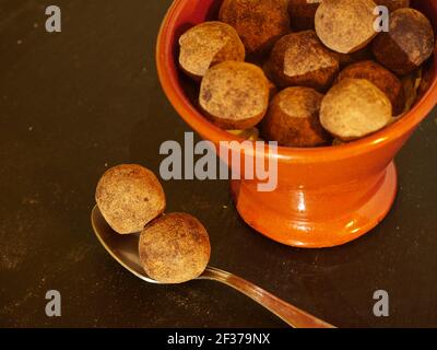 Schokoladentrüffel mit Kakaopulver im Löffel und ein Schüssel mit Trüffeln auf schwarzem Schieferbrett Stockfoto