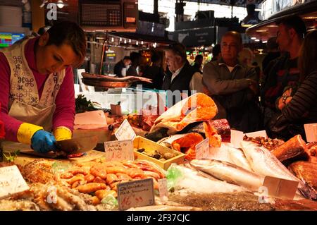 BARCELONA, SPANIEN - 10. MÄRZ 2018: Der berühmte Barcelona Lebensmittelmarkt La Boqueria. Fisch- und Meeresfrüchte-Stand. Selektiver Fokus auf Verkäufer Frau schneiden Fisch für Stockfoto