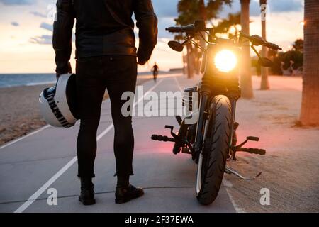 Junger Mann stehen in der Nähe von Motorrad und Blick auf den Sonnenuntergang genießen Stockfoto