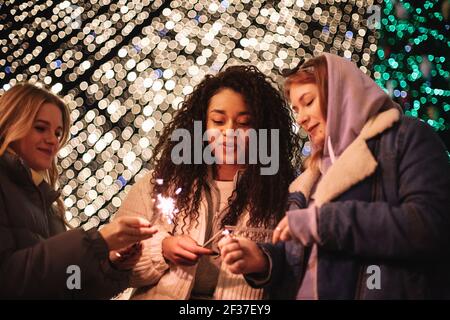 Glückliche Freundinnen zünden Funkeln, die bei weihnachtslichtern stehen Stockfoto