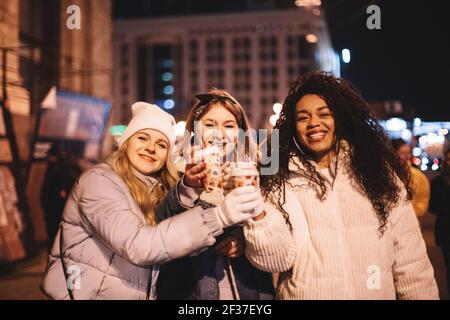 Glückliche Freundinnen, die im Winter in der Stadt heiße Getränke toasten Stockfoto