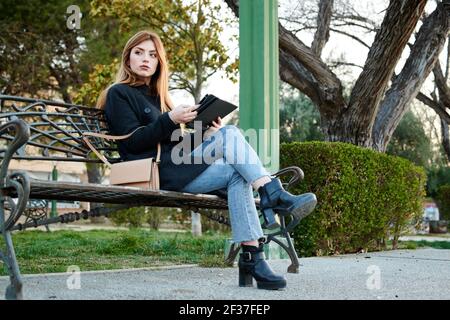 Eine attraktive junge Frau schaut sich ihr Tablet an Ein Park Stockfoto