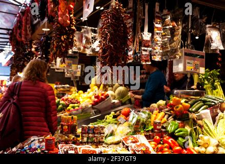 BARCELONA, SPANIEN - 10. MÄRZ 2018: Die Frau wählt einen Gemüsehändler am berühmten Barcelona Lebensmittelmarkt La Boqueria. Selektiver Fokus auf hängendes Smal Stockfoto