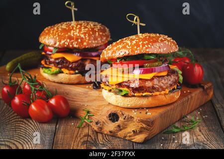 Zwei leckere hausgemachte Burger mit Rindfleisch, Käse und Gemüse auf einem alten Holztisch. Fett ungesunde Lebensmittel Nahaufnahme Stockfoto