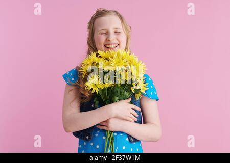 Happy modernes Kind in gepunkteten blauen Overall mit gelben Chrysanthemen Blumen vor rosa Hintergrund. Stockfoto