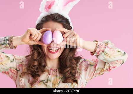 Stilvolle Frau mittleren Alters mit langen welligen Brünette Haar mit Hasenohren und osterei isoliert auf rosa. Stockfoto